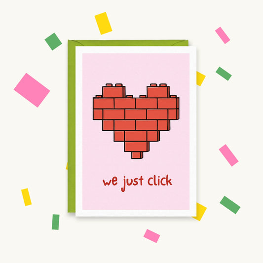 Greeting card with a red heart built from toy bricks on a pink background and the text "we just click"