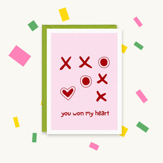 Greeting card with red noughts and crosses on pink, a heart winning the grid, and the text "you won my heart"