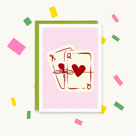 Greeting card with a king and queen of hearts playing card tied together with a red ribbon bow on a pink background