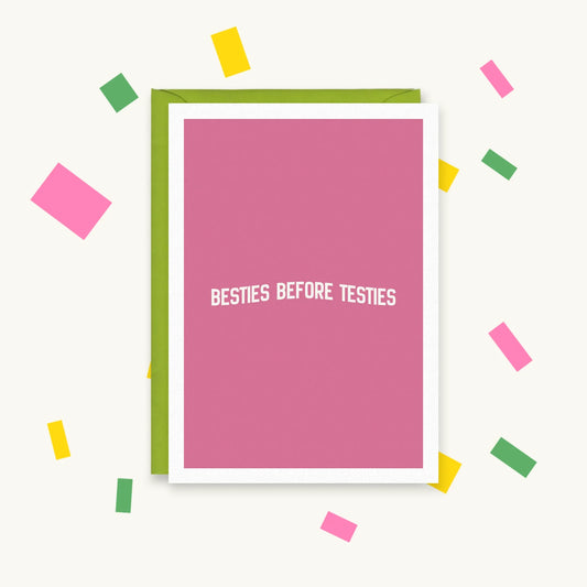 Greeting card with white arched text on a plain pink background reading "Besties Before Testies"