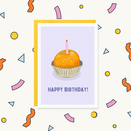 Greeting card of an orange laddoo in a paper case with a pink birthday candle, reading "Happy Birthday!"